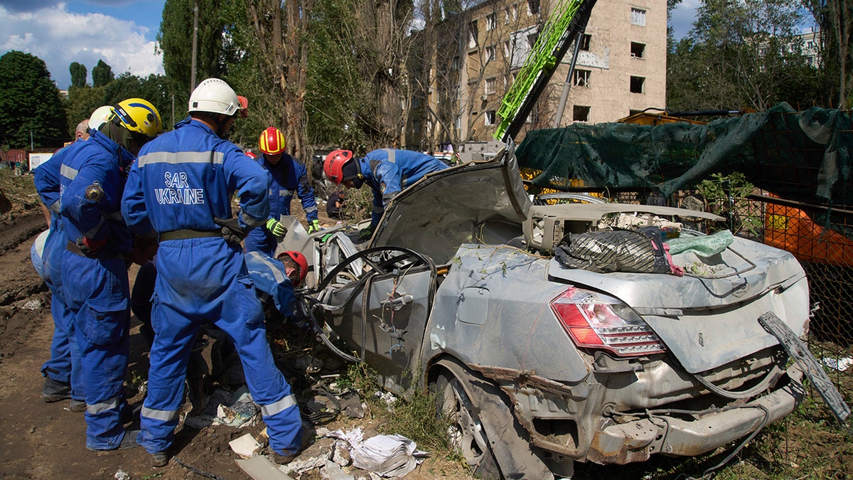 Emergency workers inspect a damaged car close to the multi-storey residential house that was ruined by a Russian missile Thursday night, killing 31 civilians including five children, in Kyiv, Ukraine, Friday, Aug. 1, 2025.(AP Photo/Efrem Lukatsky)